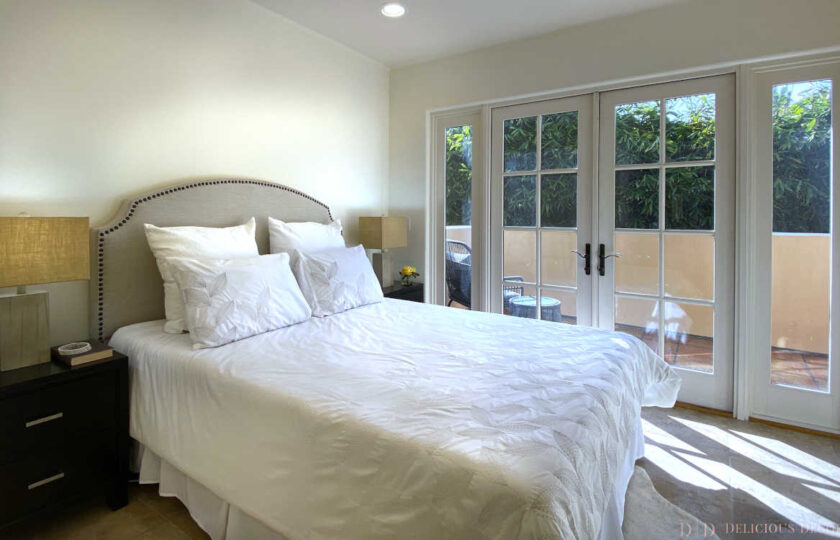 Guest bedroom facing Queen Bed with beige fabric headboard, white bedding, and outdoor patio behind