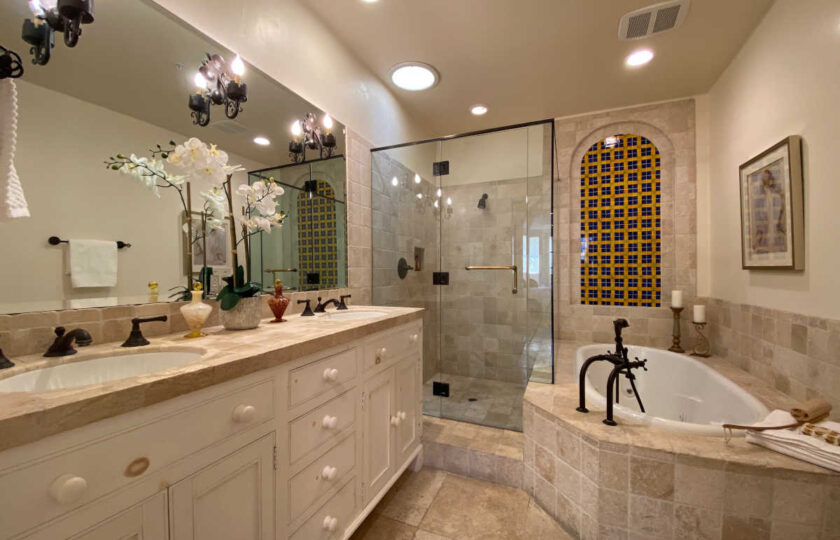 Zoomed out shot of master bathroom, showing traditional sconces, countertops, and orchids