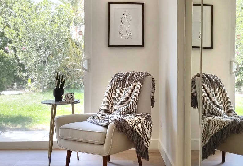 Master bedroom seating area with cream colored mid-century modern armless chair, and naked lady art above