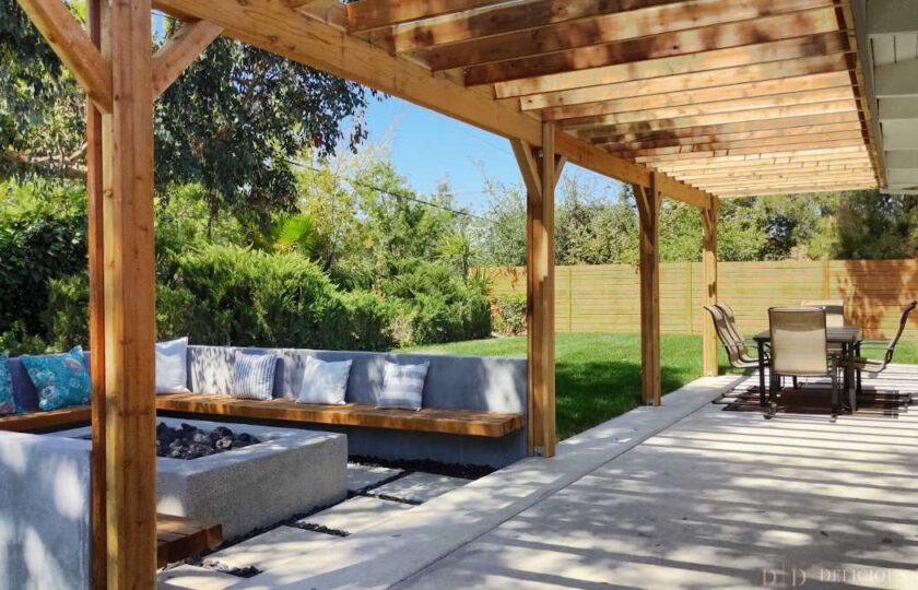 Main outdoor patio area with large wood overhang, fireplace and bench seating off to the left, and dining area to the right