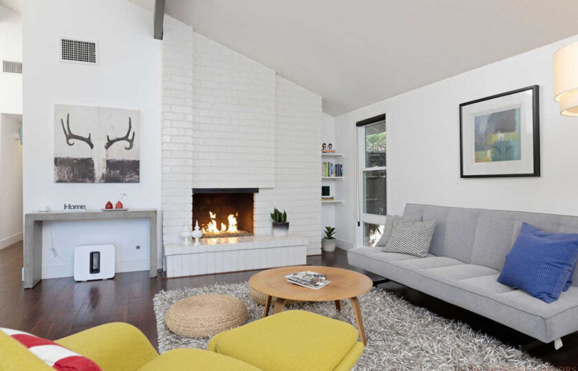Mid century modern living room scene facing grey sofa, round wood coffee table, and fireplace