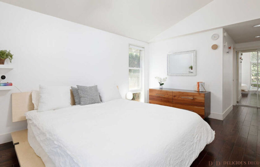 Master bedroom with light wood platform bed, white comforter, and walnut dresser