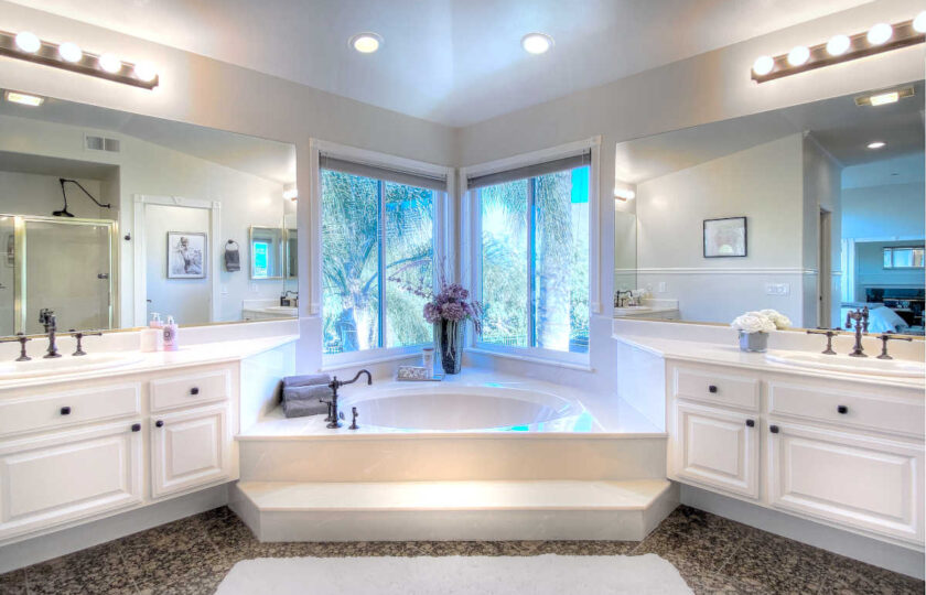 Master bathroom facing a tub between two vanities, with towels and flowers on the tub rim