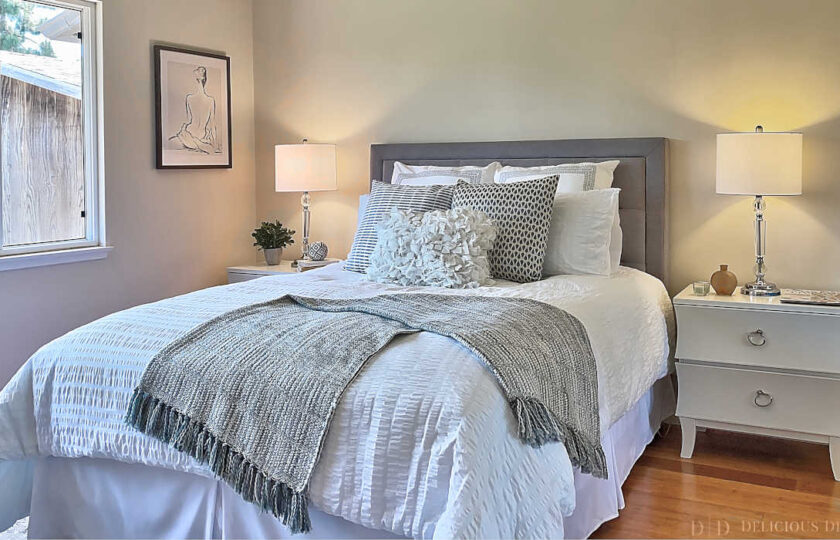 Primary bedroom home staging with grey tufted headboard, white wood nightstands, and glass lamps