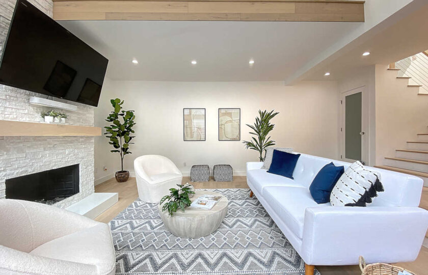 Side view of living room home staging, with a white mid-mod couch on the right and two faux shearling swivel barrel chairs