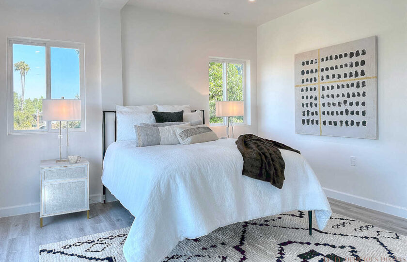 The simple black metal slatted bed with white bedding, Moroccan area rug, and traditional crystal table lamps over distressed, nightstands combine to create the perfect backdrop to make the art pop!