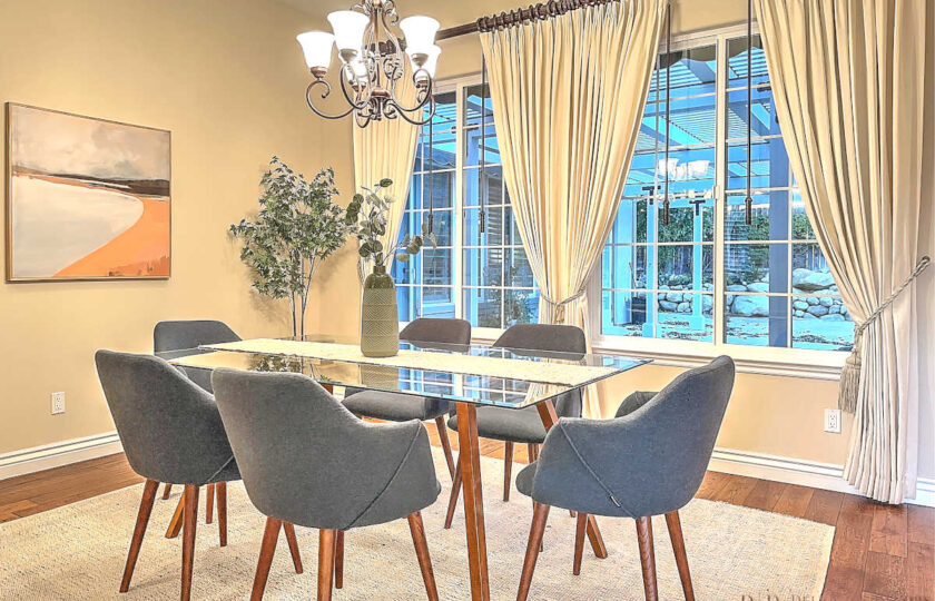 Dining room home staging with mid-century modern, glass-top dining table and navy blue dining chairs that have flared arms and splayed legs.