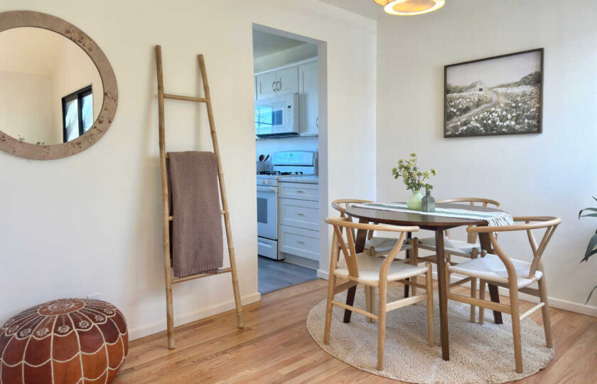 A burl wood veneer round mirror sits next to an accent ladder with leather boho pouf underneath to add interest to the dining space.