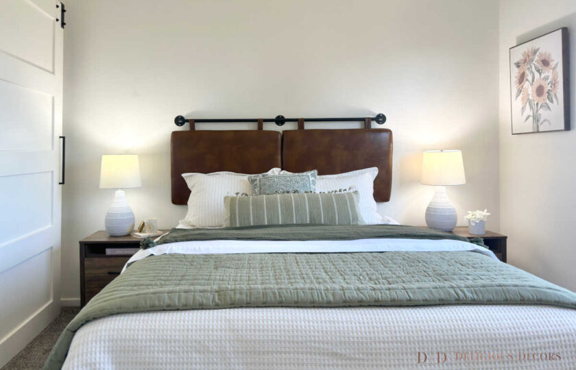 The primary bedroom home staging features a cognac leather headboard with sage green accent pillows and throw.