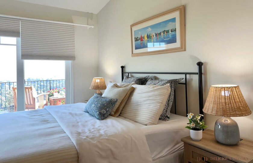 Coastal bedroom featuring a black iron bed with blue and white pillows, sailboat art, and wicker lampshades.