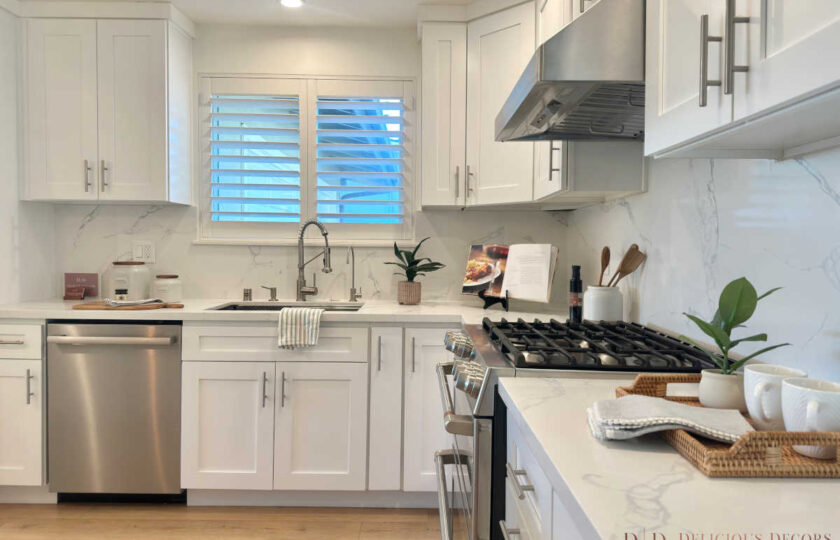 Crisp white kitchen styling showcasing marble-veined quartz countertops, stainless steel appliances, and plantation shutters over a farmhouse sink.
