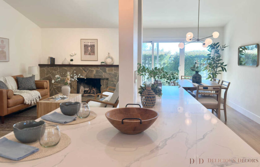 View from a kitchen island into an open-concept living and dining area staged with relaxed, organic textures and warm leather seating.