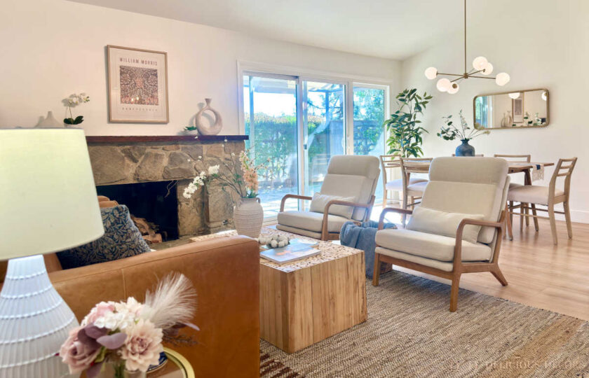 California Casual open-concept living and dining space styled with a textured jute rug, mid-century globe chandelier, and light oak dining table looking out to a lush backyard.