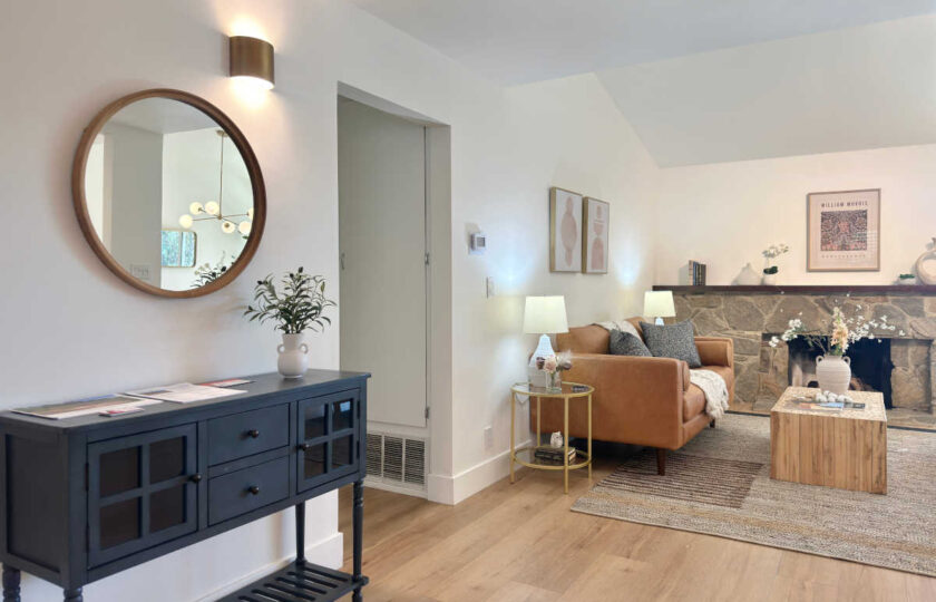 Stylish entryway drop zone featuring a dark slatted console table and a round wood-framed mirror leading into a bright, open living room.