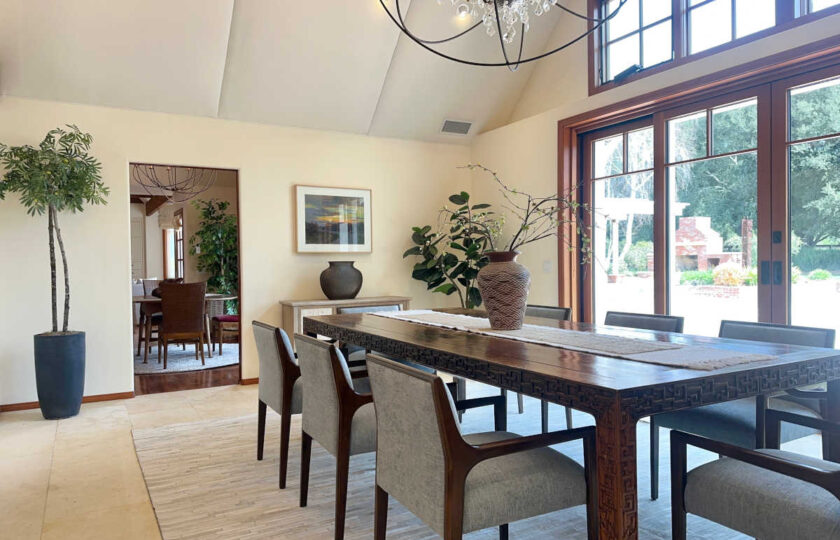 Santa Ynez luxury estate staging in a bright formal dining room featuring a long carved wood table and grey linen chairs looking out through glass doors to the equestrian grounds.