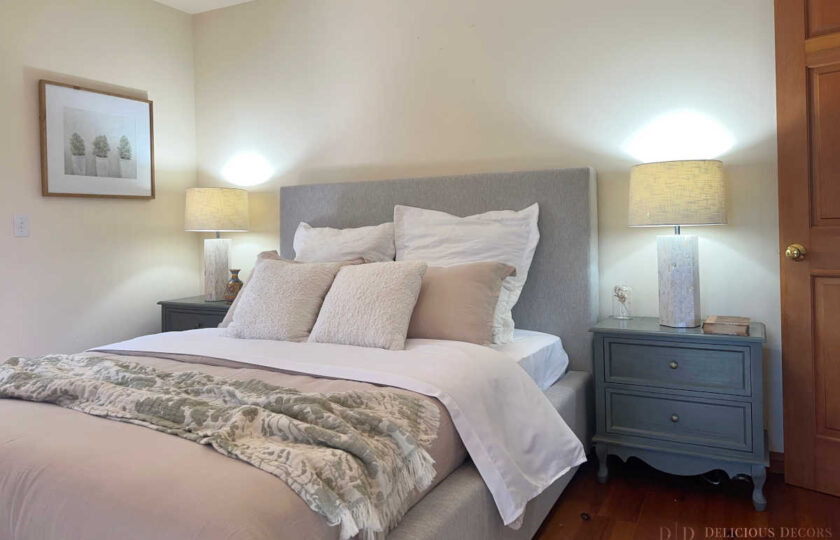 Guest bedroom staging highlighting a soft grey upholstered bed, textured accent pillows, and dark nightstands paired with decorative table lamps.