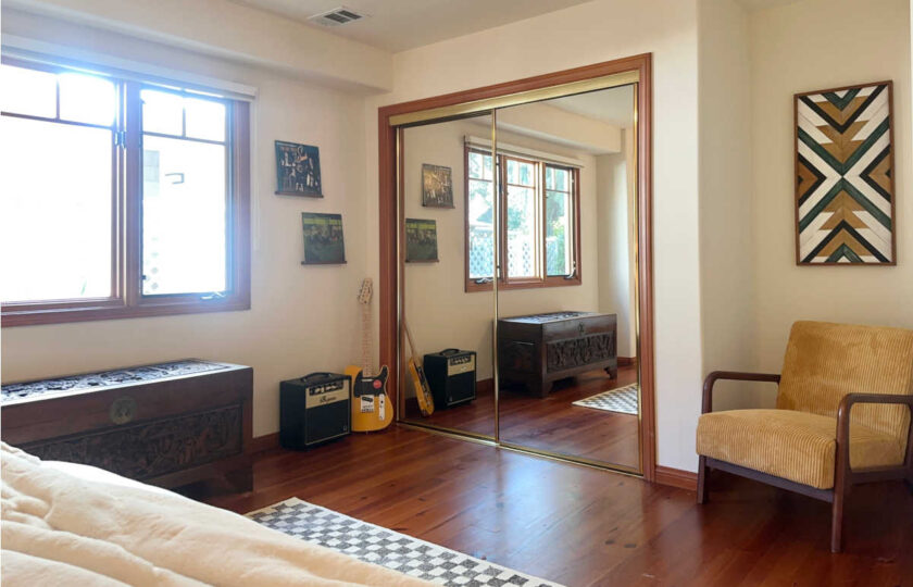 Santa Ynez luxury estate staging in the moody "his" suite styled with a mustard yellow corduroy chair and vintage guitars, accented by a heavy carved wood trunk and mirrored closet doors.