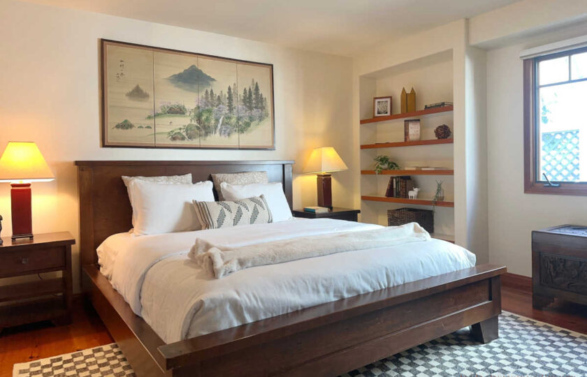 Santa Ynez luxury estate staging in a guest bedroom featuring a heavy dark wood bed, symmetrical nightstands with warm lighting, and custom built-in wall shelving.