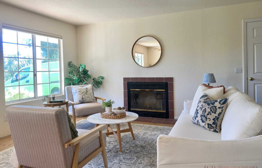Standalone guest house living room staged with a cottage-inspired design, featuring a white slipcovered sofa, a round mirror, and a cozy fireplace as part of a Santa Ynez luxury estate staging.