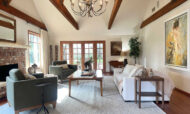 Santa Ynez luxury estate staging featuring massive timber trusses , wide-plank floors, a red brick fireplace, and deep olive green velvet armchairs arranged around an oversized knotty wood coffee table.