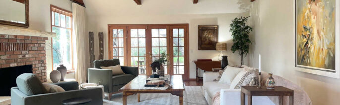 Santa Ynez luxury estate staging featuring massive timber trusses , wide-plank floors, a red brick fireplace, and deep olive green velvet armchairs arranged around an oversized knotty wood coffee table.