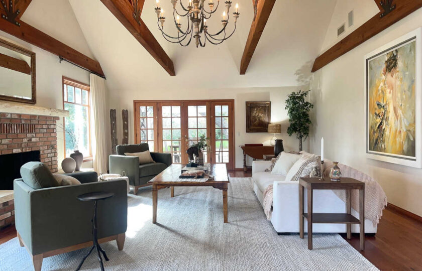 Santa Ynez luxury estate staging featuring massive timber trusses , wide-plank floors, a red brick fireplace, and deep olive green velvet armchairs arranged around an oversized knotty wood coffee table.