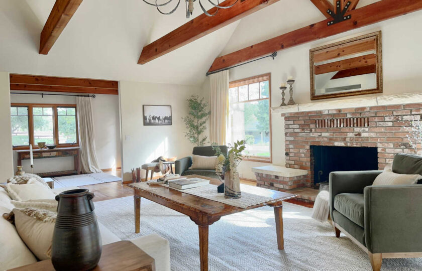 Rustic luxury living room featuring wide-plank floors, a red brick fireplace with a stone mantel, and deep green velvet armchairs centered around a rustic wood coffee table.