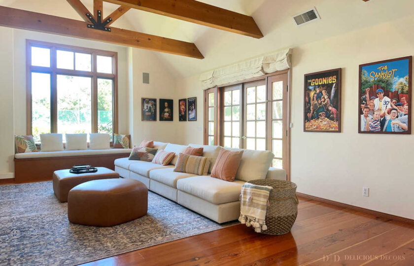 Expansive media room staging ready for movie nights with a deep cream linen sectional and dual tan leather ottomans positioned below classic movie posters.