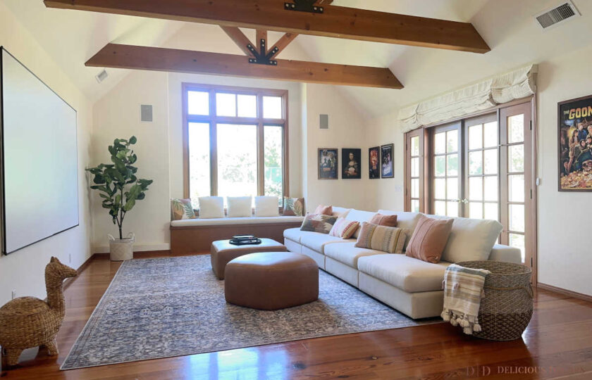 Santa Ynez luxury estate staging in an expansive media room featuring a large projector screen, exposed timber trusses, a cream linen sectional, and dual tan leather ottomans.