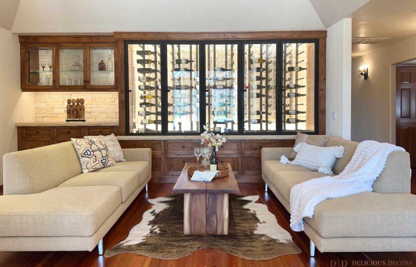 Symmetrical staging in a custom wine tasting room featuring oatmeal linen sofas , a raw-edge walnut coffee table , and a natural cowhide rug in front of a beautifully illuminated wine display.