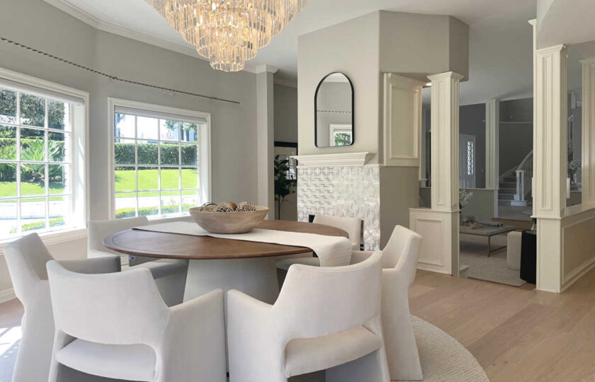 Modern transitional formal dining room with round wood table, white armchairs, crystal chandelier, and tiled fireplace.