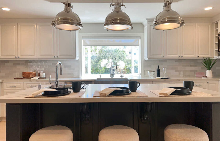Luxury staged kitchen featuring dark island with travertine countertop, bouclé counter stools, and industrial pendant lights.