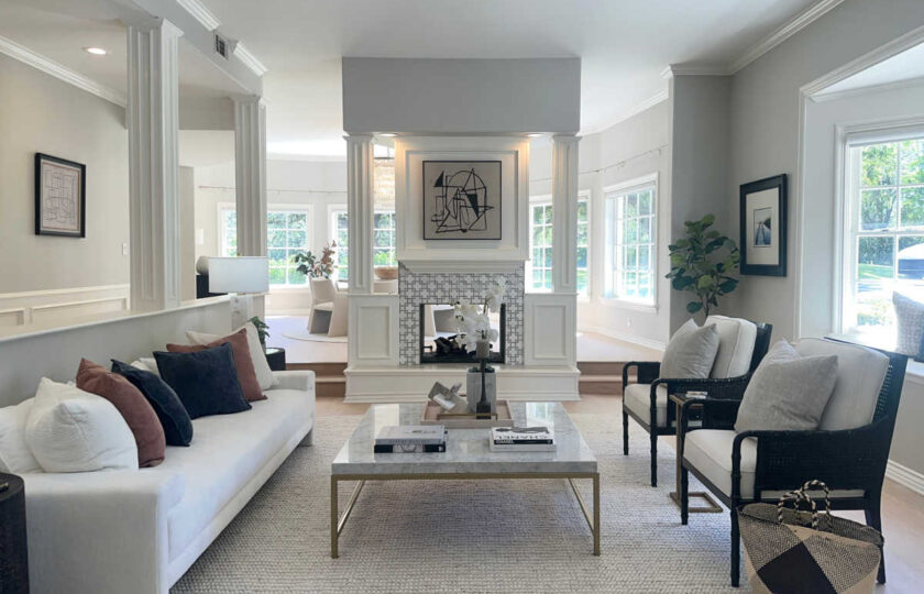 Modern transitional staging in Westlake Village formal living room featuring dual-sided fireplace, white sofa, and black accent chairs.