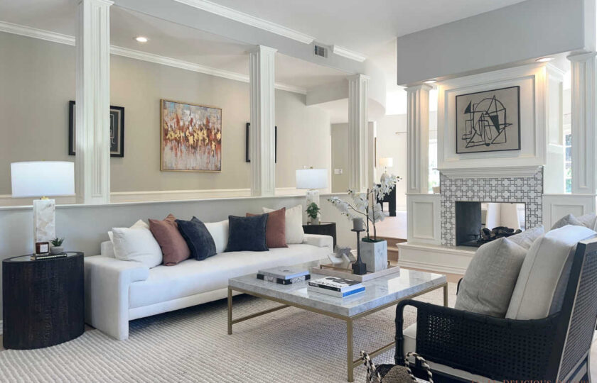 Staged formal living room showcasing white custom sofa with rust accent pillows, marble coffee table, and architectural columns.