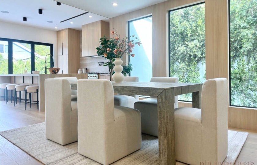 North Hollywood modern organic staging in a dining area featuring a light gray wood dining table, upholstered chairs, an open view to the kitchen, and a custom wall-mounted wine rack.