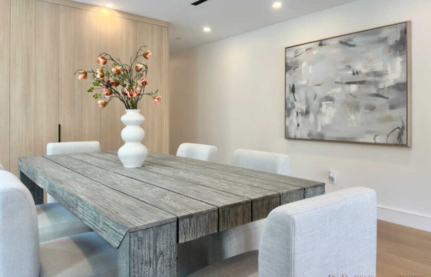 Modern organic dining room staging highlighting a gray wood table paired with a ceramic sculptural vase, floral branches, and large abstract canvas art.