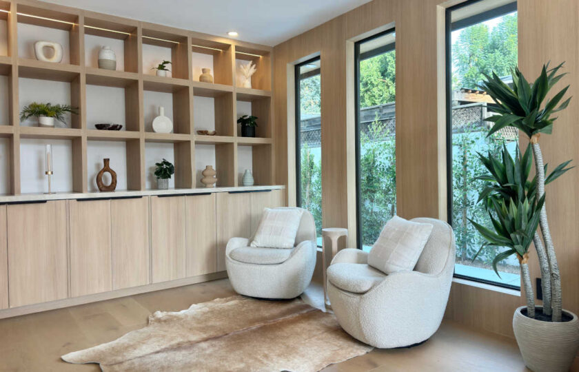 Modern organic staging in a lounge nook featuring custom light oak shelving filled with neutral ceramics, white bouclé swivel chairs, and a natural cowhide rug.