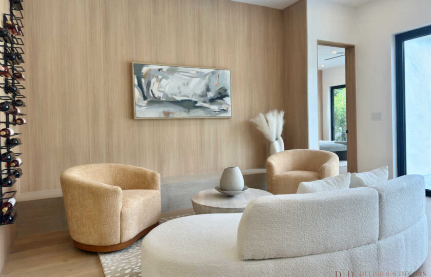 Living room staging showcasing warm wood paneling, abstract canvas art, pampas grass decor, and a white curved bouclé couch.