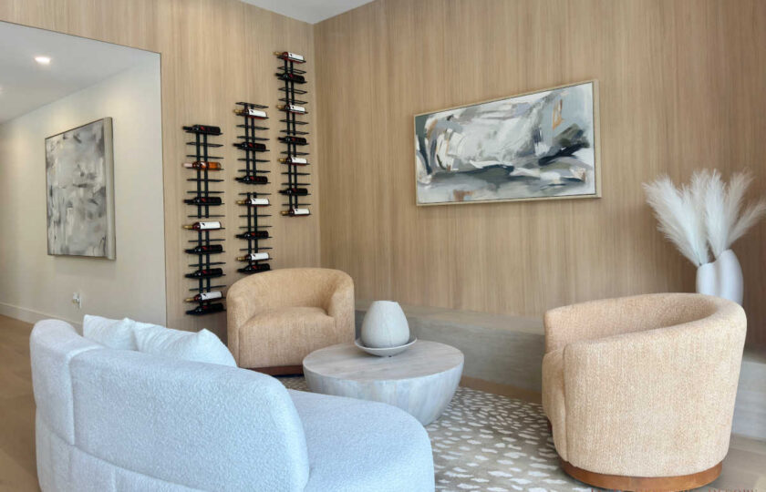 Staged family room featuring a curved white bouclé sofa, tan barrel chairs, a round wood coffee table, and a wall-mounted wine rack.