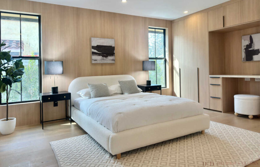 Guest bedroom staged in a modern organic aesthetic with a white bouclé bed, black nightstands, light oak wall paneling, and a geometric area rug.