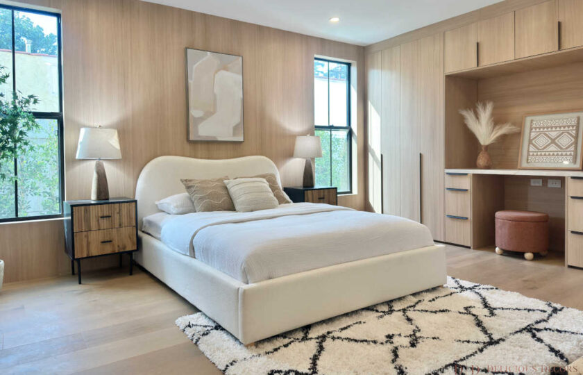 Bedroom suite featuring light oak built-in cabinetry, a vanity desk nook, woven accent benches, and a round wall mirror.