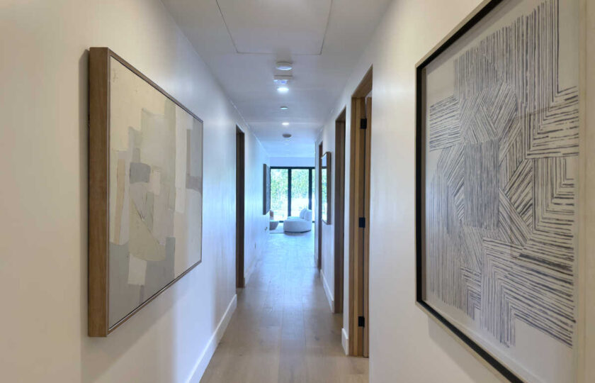 Modern organic home hallway staged with neutral abstract canvas artwork, light hardwood floors, and recessed ceiling lighting.