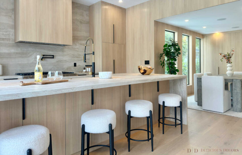 Wide shot of a staged kitchen island with bouclé barstools, wine glasses, and an open layout leading into the dining space.