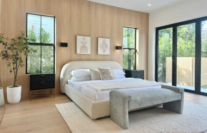 Primary bedroom staged in a modern organic style with a curved bouclé bed, textured end bench, black nightstands, and light wood accent wall.