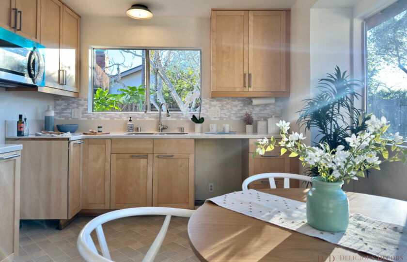 Bright kitchen staging featuring light maple wood cabinets, mosaic tile backsplash, garden window over the sink, and adjacent sunlit dining nook.