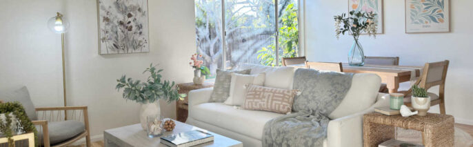 California Casual open-concept living and dining space styled with a white slipcovered sofa, light oak dining set, woven seagrass end table, and botanical wall art.