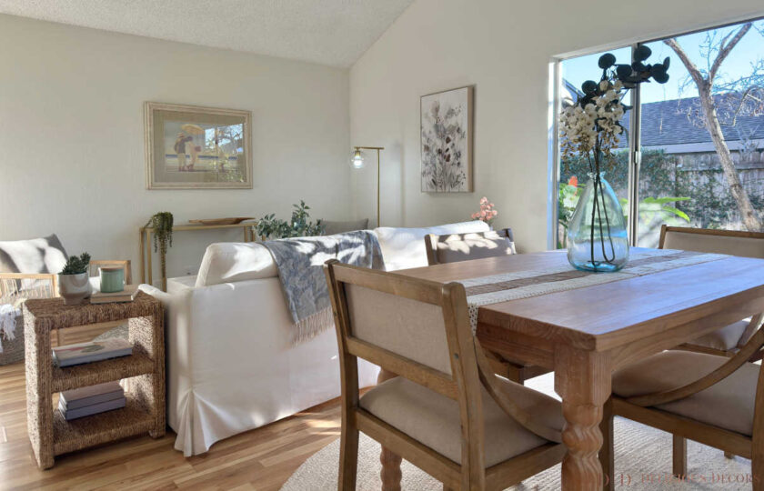 Open dining area featuring a natural wooden dining table, neutral upholstered chairs, glass botanical vase, and sliding glass garden door.