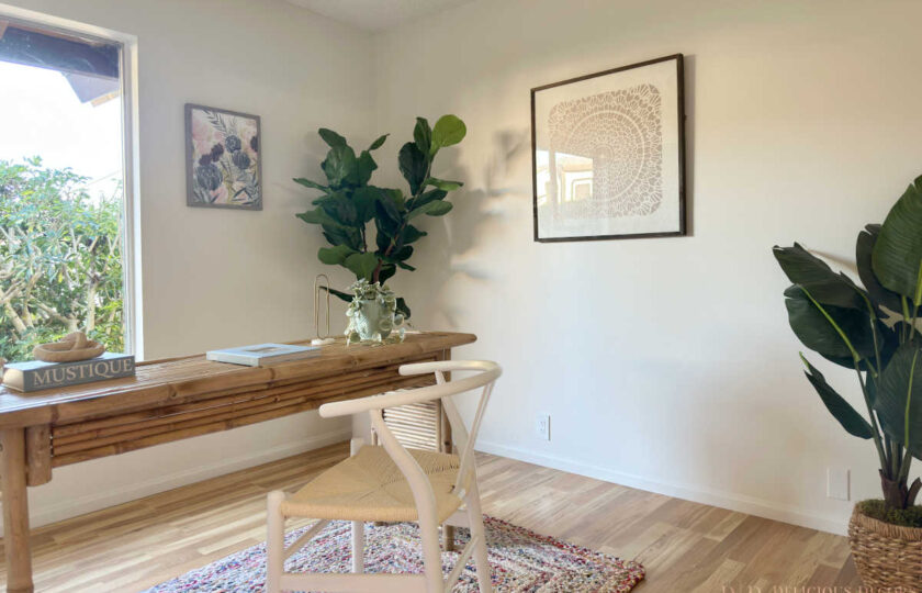 Staged dedicated home office featuring a slatted bamboo desk, white woven wishbone chair, colorful rug, potted fiddle leaf fig, and textured wall art.