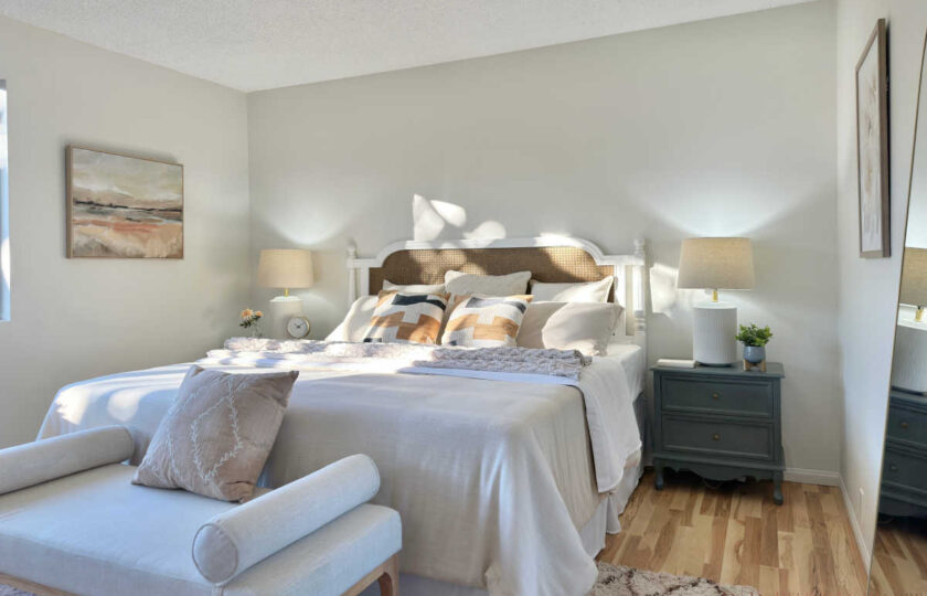 Serene primary bedroom staging styled with a woven cane headboard bed, neutral bedding, charcoal grey nightstands, and soft morning light.