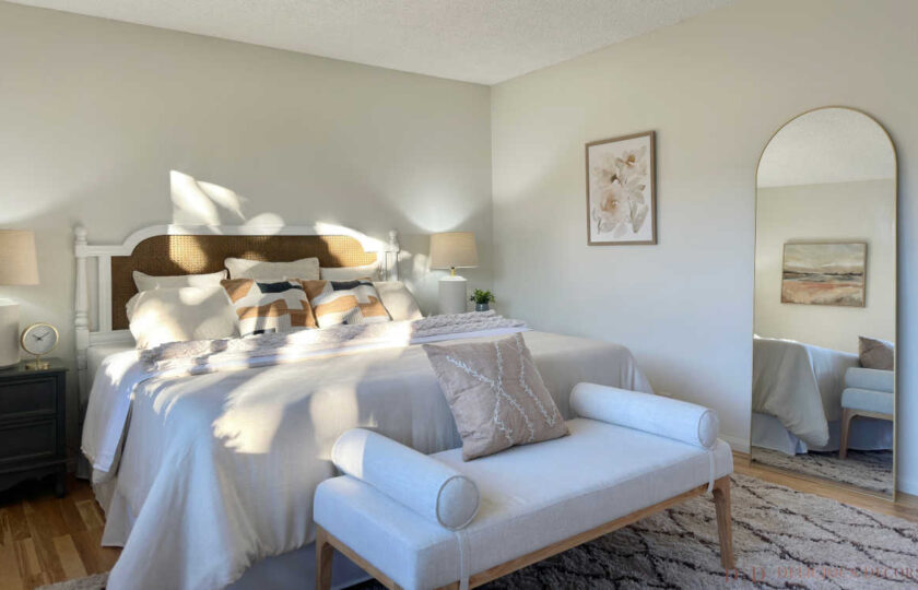 Sunlit primary bedroom detail featuring an arched gold leaning floor mirror, upholstered bench at the foot of the bed, and plush diamond shag rug.